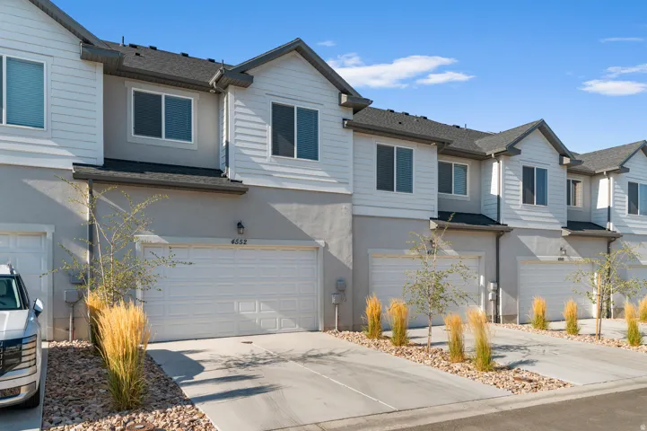Contemporary townhome community featuring modern architectural design with clean-lined white exterior siding, two-car garage with white paneled doors, and professionally landscaped front grounds