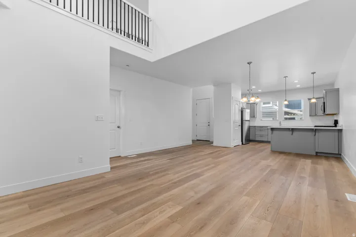 Open-concept living area with wood-finish flooring, a two-story ceiling, and an upper-level balcony with black metal railings