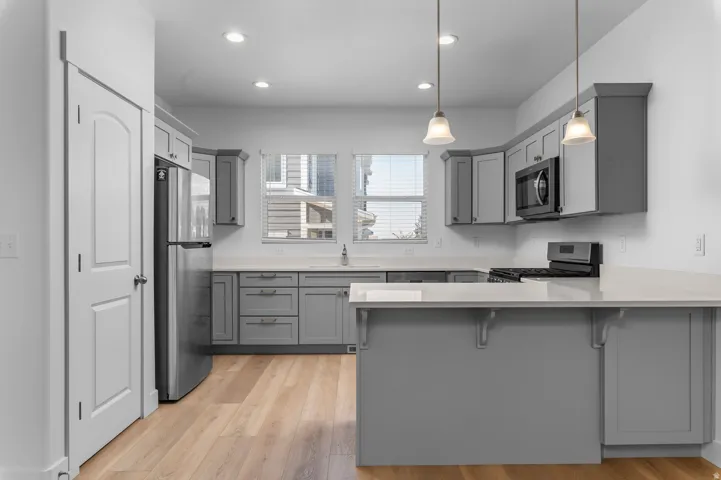 Modern kitchen featuring wood-finish flooring, grey cabinetry, light-toned countertops, stainless steel appliances, and recessed lighting