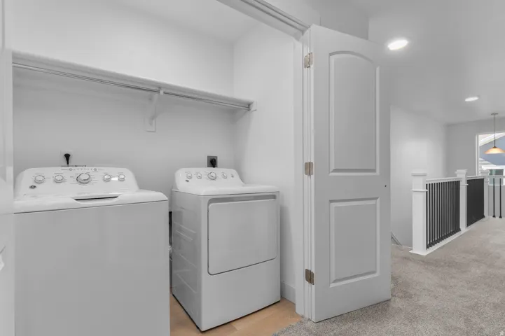 Dedicated laundry room featuring side-by-side front-load washer and electric dryer with full-size capacity, chrome rod shelving for storage, recessed ceiling lighting, and direct access to additional living spaces