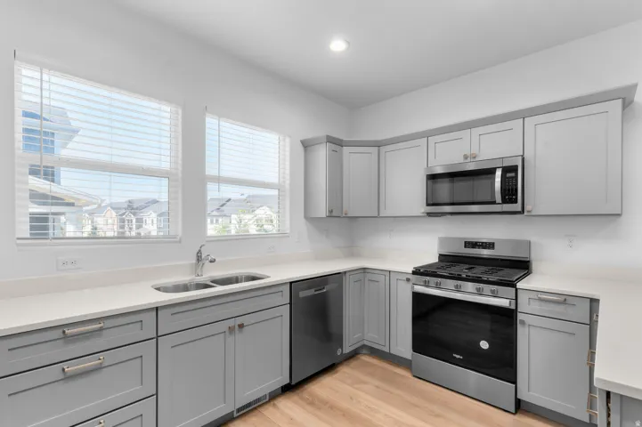 Kitchen featuring light wood-finish flooring, light grey cabinetry, stainless steel appliances, a double basin sink, and ample countertop space