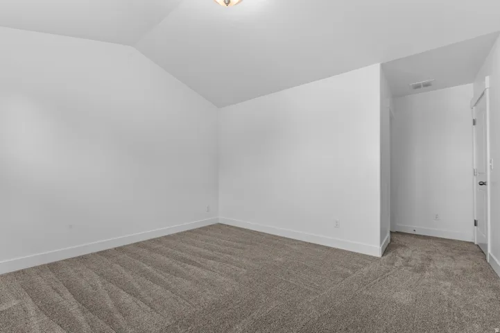 Carpeted room featuring a vaulted ceiling, white walls, and bright overhead lighting
