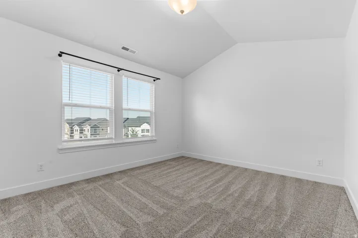 Carpeted interior space featuring white walls and a vaulted ceiling