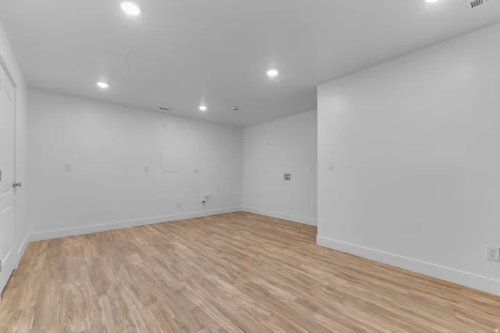 Spacious room featuring wood-finish flooring, recessed ceiling lighting, crisp white walls, and bright white baseboards