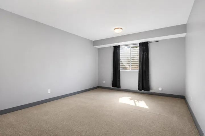 Carpeted room featuring light gray walls, dark gray baseboards, and a window with black curtains