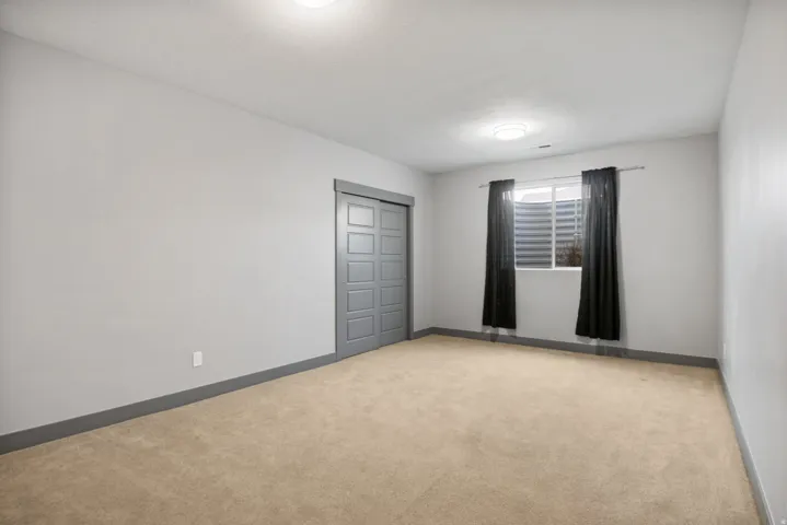 Carpeted room with light gray walls, dark gray baseboards, and a window featuring a window well