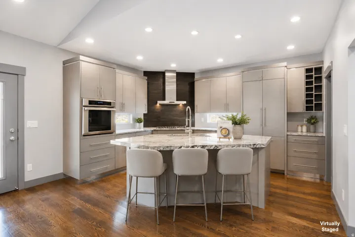 Gourmet kitchen featuring a large central island with seating, stainless steel appliances, contemporary cabinetry, a built-in wine rack, and rich wood-finish flooring