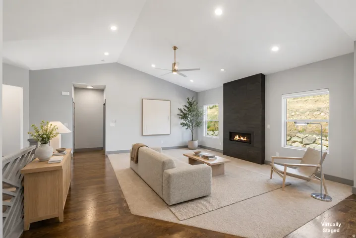 Sophisticated living space showcasing a soaring vaulted ceiling with recessed lighting, wide-plank wood-finish flooring, and a striking floor-to-ceiling black fireplace accent wall