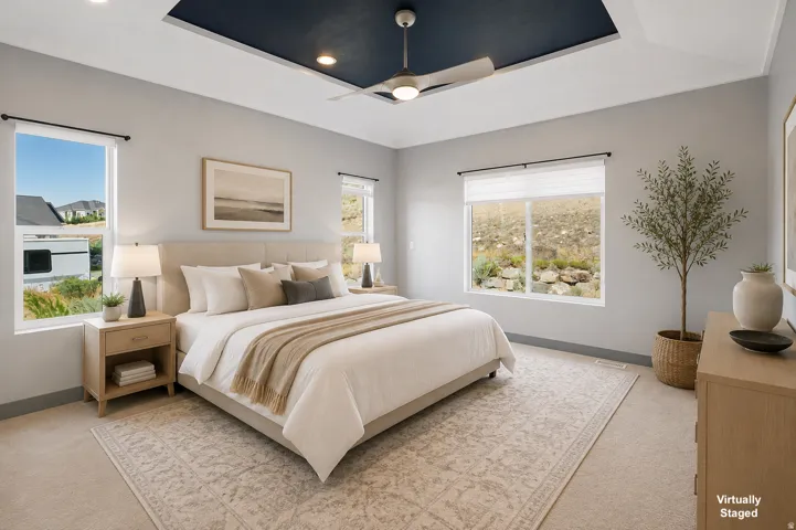 Spacious primary bedroom showcasing a coffered ceiling with recessed lighting, abundant natural light from multiple windows, light wood-finish nightstands with integrated storage, neutral color palette with layered bedding in cream and taupe tones, and a