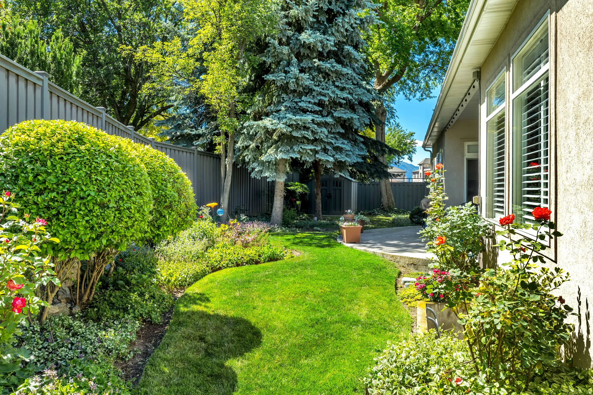 Private backyard featuring a manicured lawn, established landscaping, mature trees, and storage shed