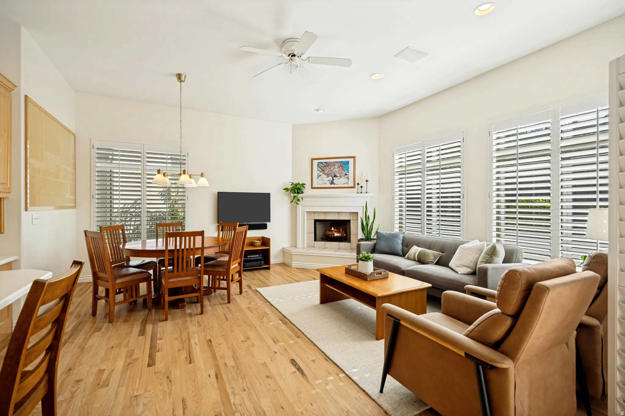 Open-concept living and dining area featuring oak hardwood flooring, a corner fireplace, and multiple windows with white plantation shutters
