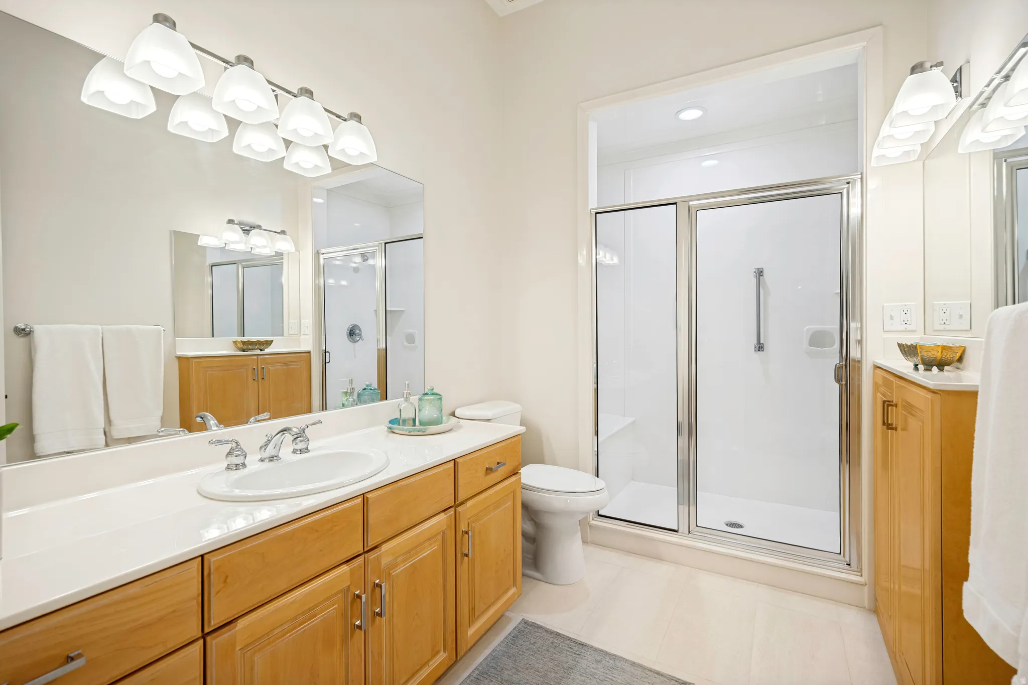 Second ensuite bathroom featuring a wide vanity with a single basin, maple cabinetry, white countertop, and a large mirror