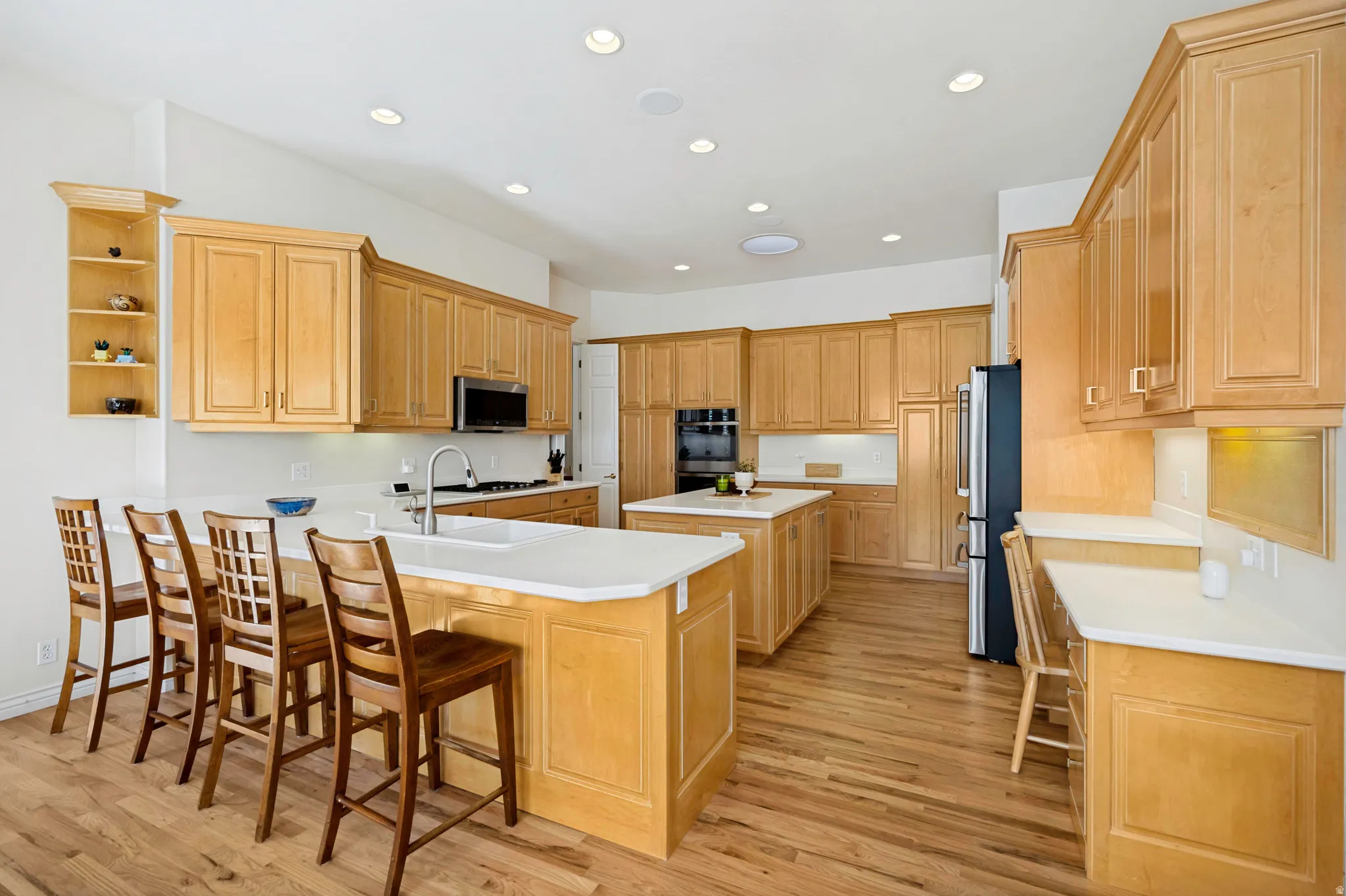 Spacious kitchen featuring maple cabinetry throughout, a large center island with seating for multiple guests, stainless steel appliances, recessed ceiling lighting, and oak hardwood flooring