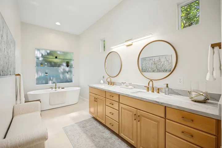 Bright bathroom featuring a freestanding soaking tub, a double vanity with maple cabinetry, and a quartz stone countertop