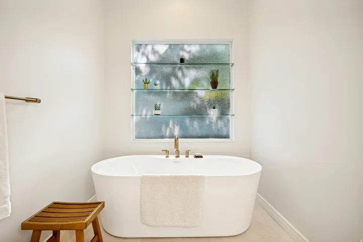 Spa-inspired primary bathroom featuring a freestanding soaking tub with clean lines, polished brass fixtures, and a muted window and skylight, inviting natural light.