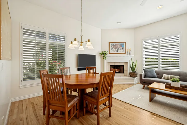 Open-concept living area featuring oak hardwood flooring, a corner fireplace with a detailed mantel, and multiple windows fitted with white plantation shutters