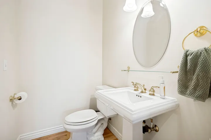 Main level powder room pedestal sink with brass-finish faucet, oval mirror, and wall-mounted vanity lighting