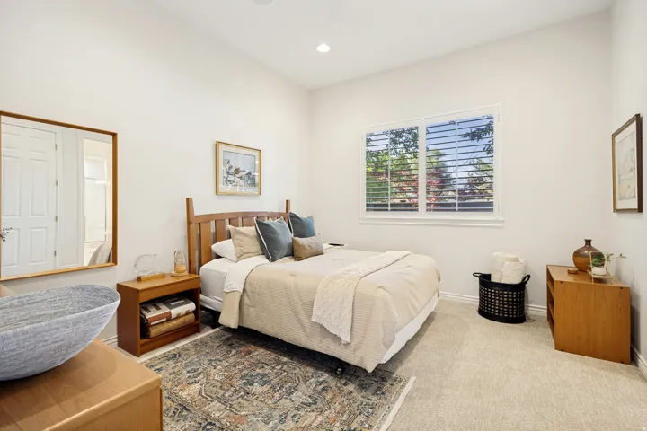 Carpeted second bedroom room featuring a large window with plantation shutters, recessed lighting, and en suite bathroom