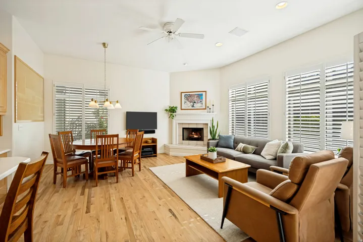 Open-concept living and dining area featuring oak hardwood flooring, a corner fireplace, and multiple windows with white plantation shutters