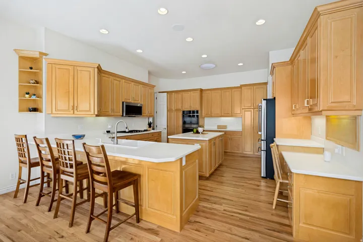 Spacious kitchen featuring maple cabinetry throughout, a large center island with seating for multiple guests, stainless steel appliances, recessed ceiling lighting, and oak hardwood flooring
