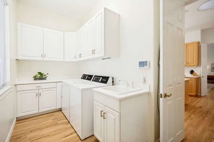 Dedicated laundry area featuring custom white cabinetry, light-toned countertops, and oak hardwood flooring