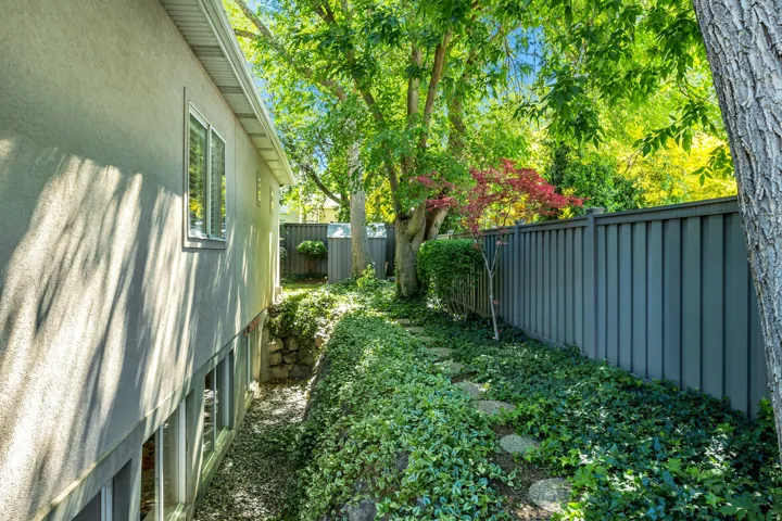 Landscaped side yard featuring a privacy fence, mature trees, ground cover, and stepping stones