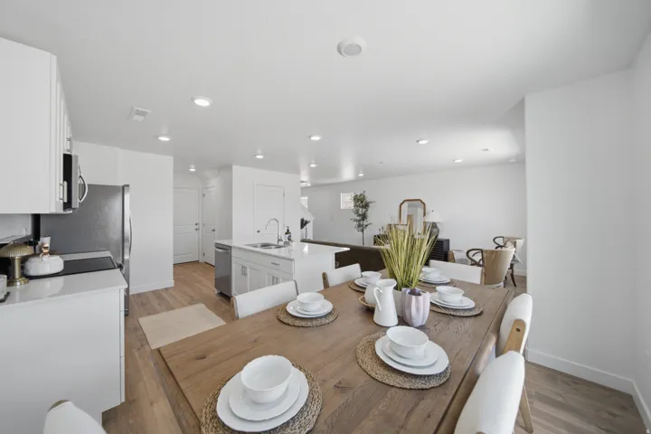 Open-concept living space with wood-finish flooring, white cabinetry, recessed lighting, a kitchen island with sink, and stainless steel appliances