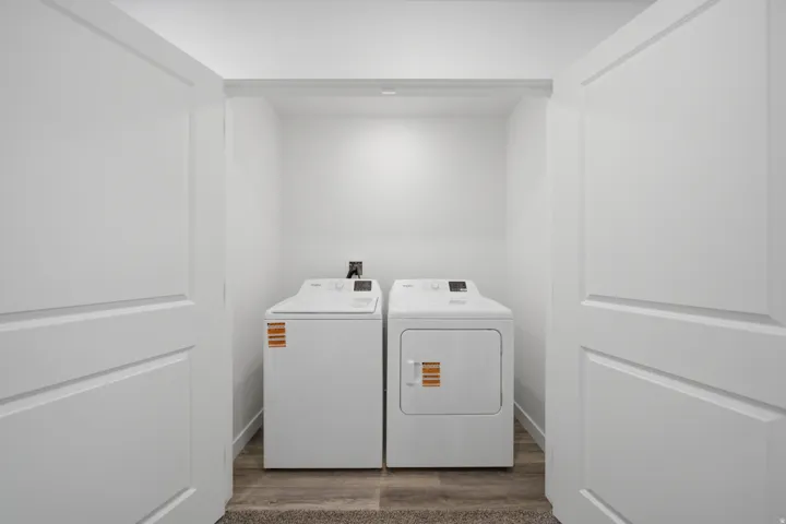 Dedicated laundry area featuring a washer and dryer unit, wood-finish flooring, and crisp white walls