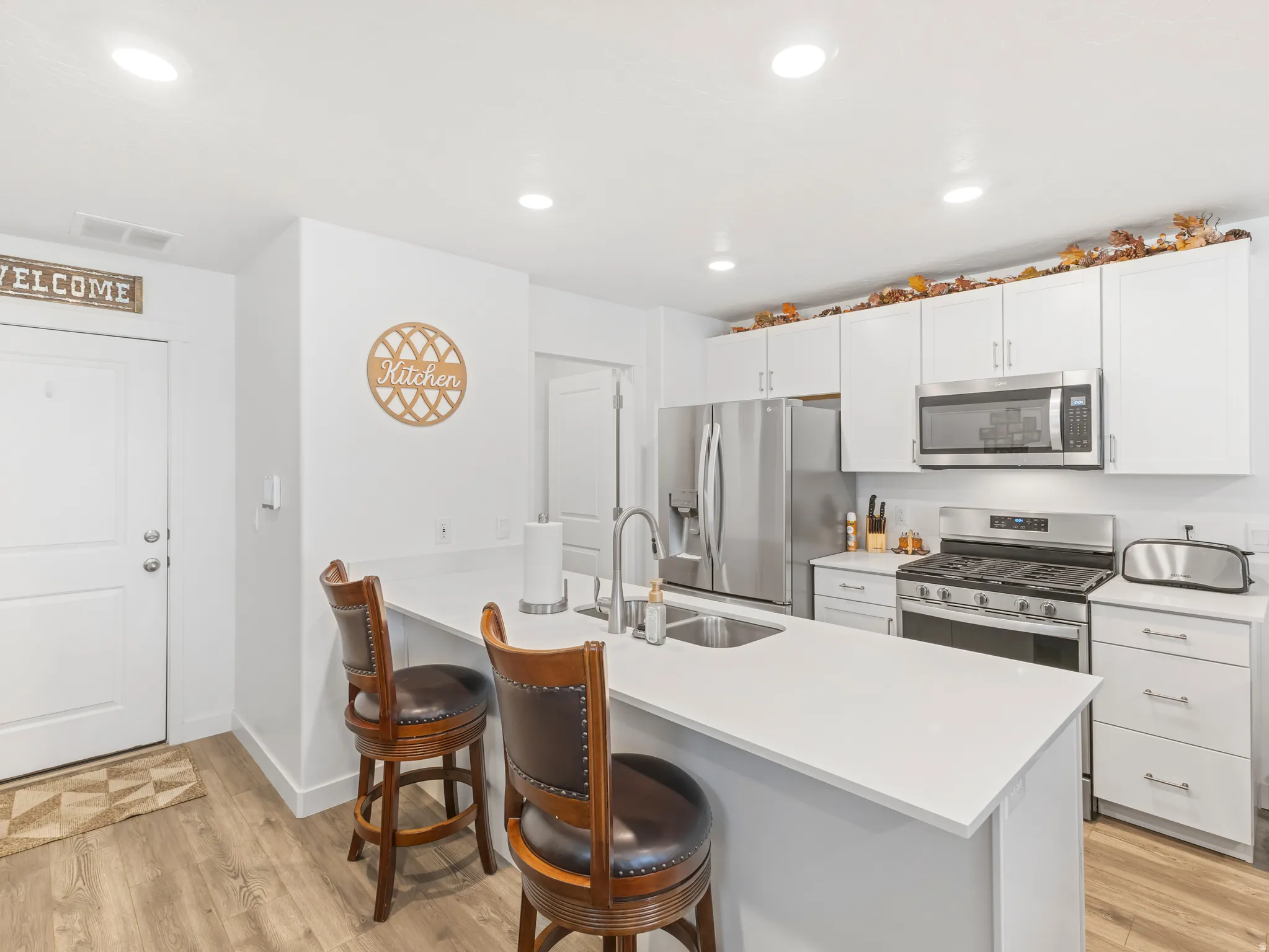 Bright kitchen featuring white cabinetry, stainless steel appliances, a white countertop island with an undermount sink, recessed lighting, and wood-finish flooring