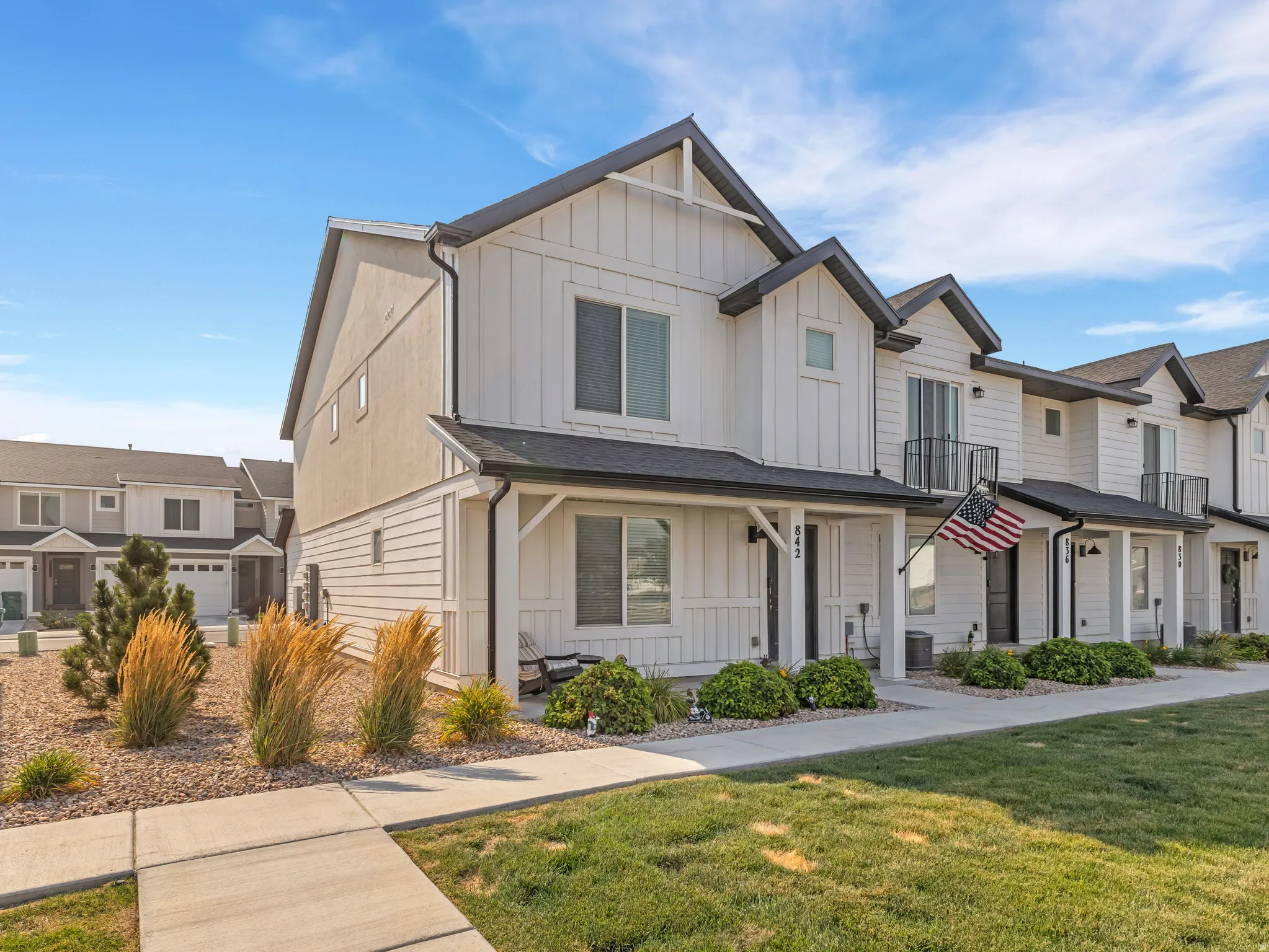 Contemporary townhome exterior featuring white board and batten siding, dark trim, and a covered front porch