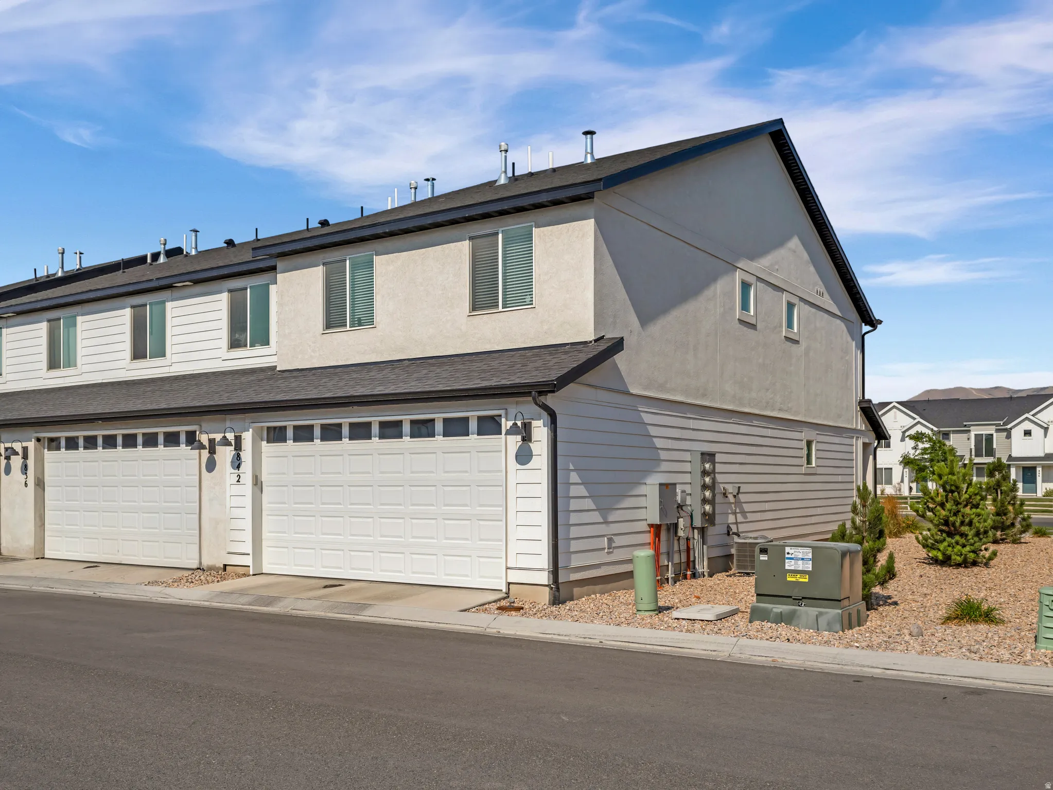 Contemporary townhome exterior featuring an attached two-car garage with paneling and transom windows, stucco and horizontal siding, and a dark asphalt shingle roof
