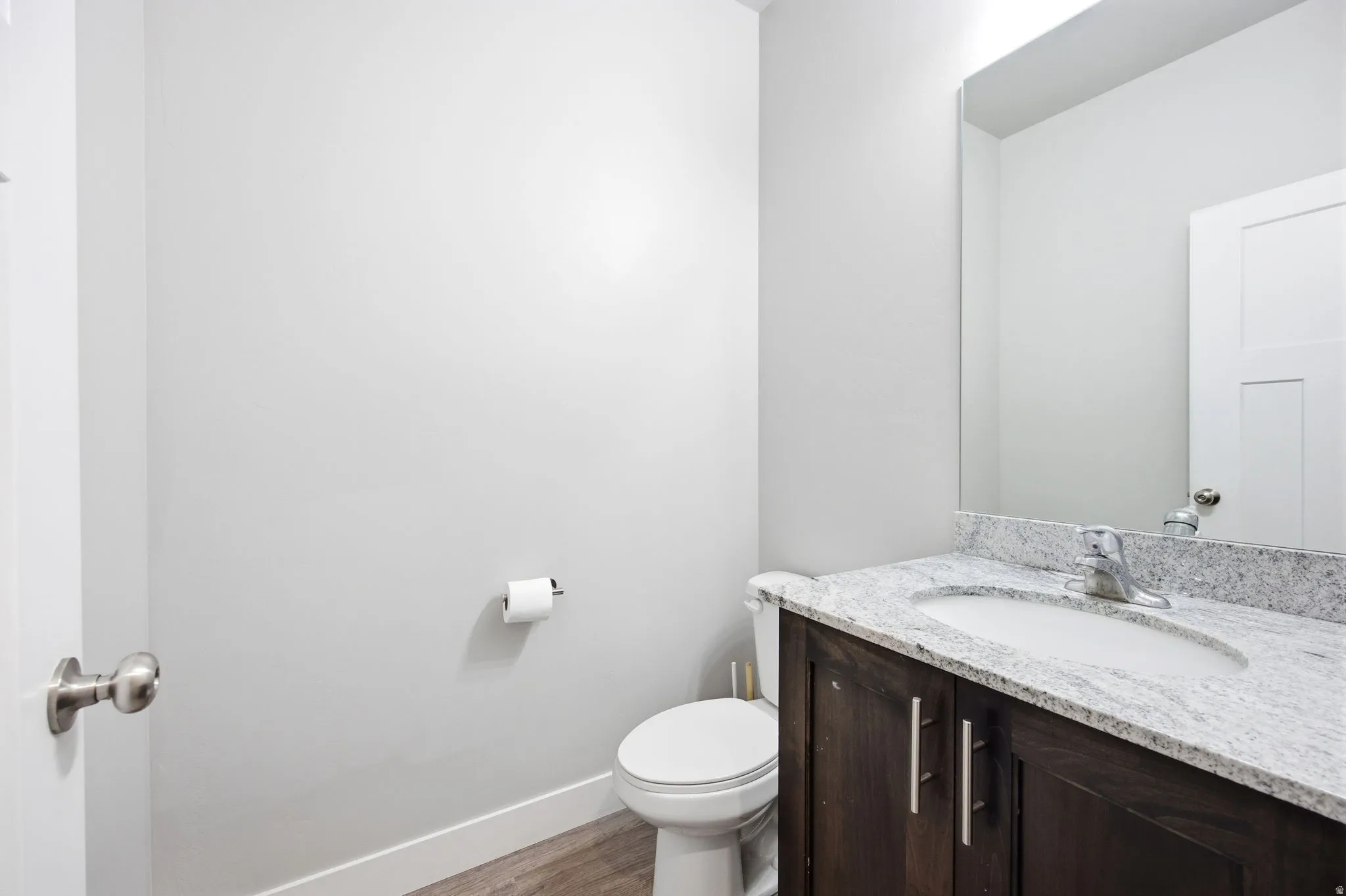 Powder room featuring a single-sink vanity with a light-toned stone countertop, wood-finish cabinetry, and a frameless mirror