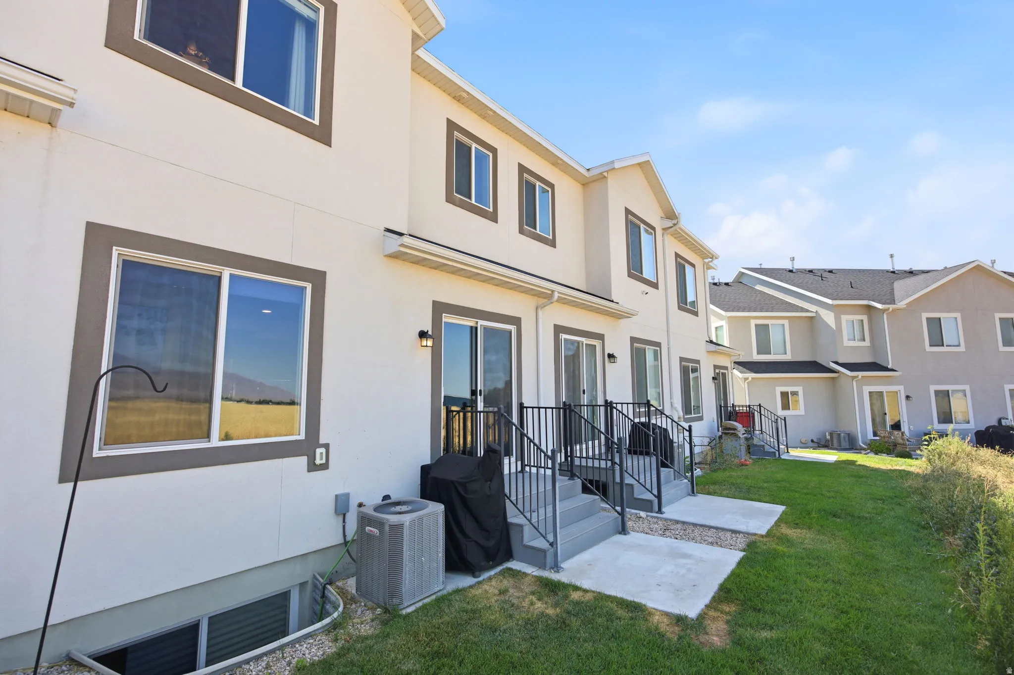 Contemporary townhome exterior featuring a clean cream and tan facade with multiple windows, black metal railings, and a welcoming entry with concrete patio