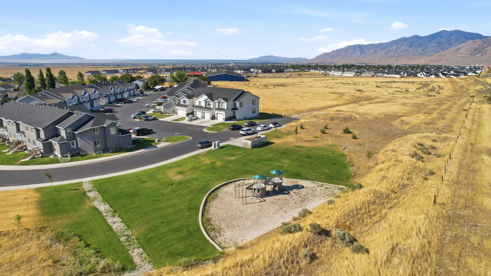 Expansive residential lot showcasing manicured lawn, circular hardscaped patio with playground equipment, and curved stone pathway