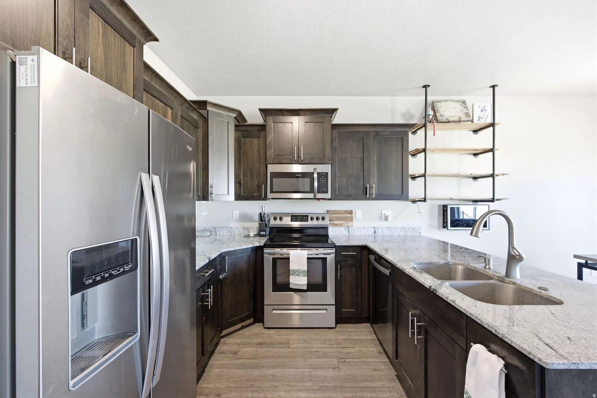 Modern kitchen featuring dark wood cabinetry, stainless steel appliances including a built-in refrigerator and range, and a large island with a gray quartz countertop and undermount sink