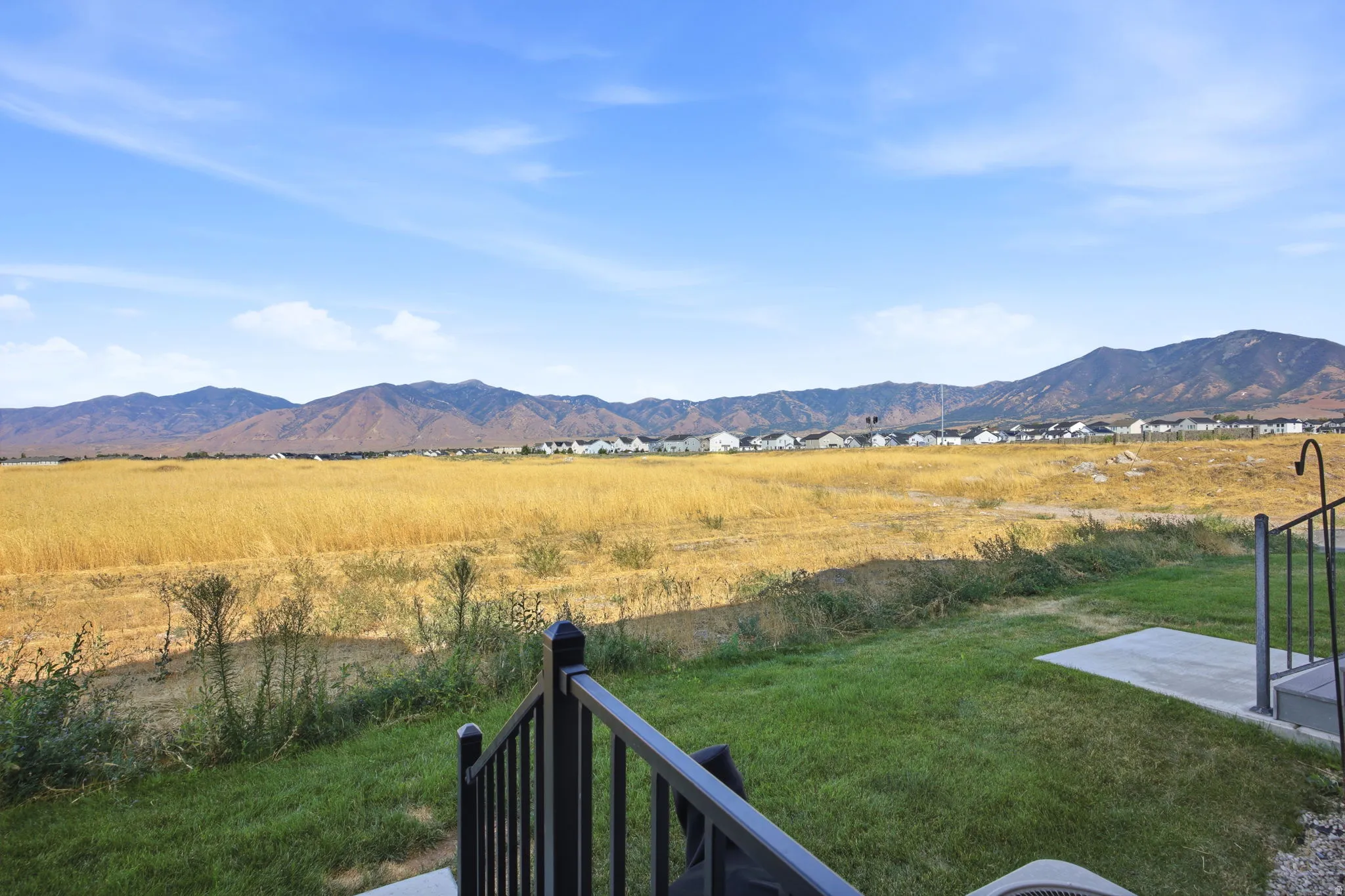 Expansive backyard with mature lawn and black metal railing, overlooking rolling grassland and distant mountain range
