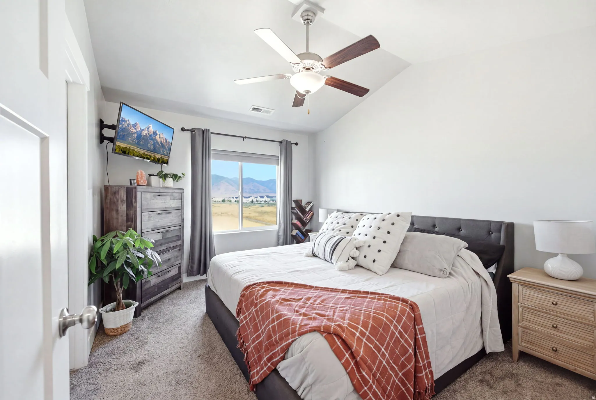 Spacious bedroom featuring a dark upholstered bed frame, wood-finish nightstands with ample storage, carpet flooring, and a ceiling fan with integrated lighting