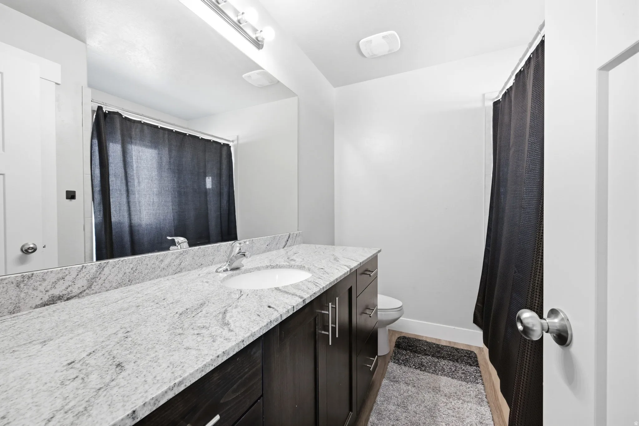 Bathroom featuring an expansive vanity with a light-toned stone countertop, an integrated sink, and dark wood-finish cabinetry
