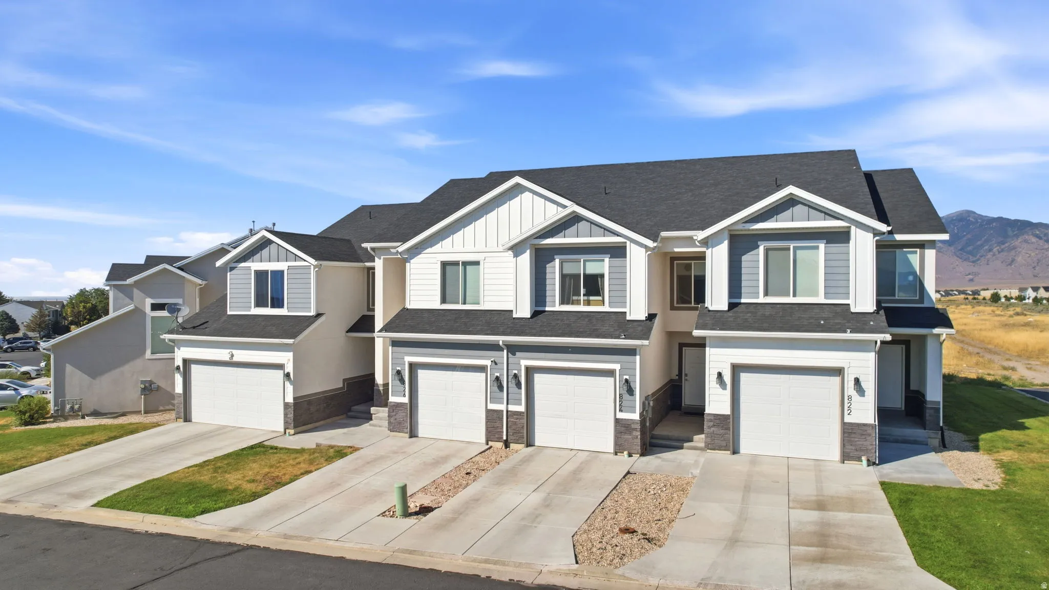 Modern townhome community featuring clean-lined architectural design with board-and-batten exterior accents, multi-unit configuration with individual two-car garages, manicured landscaping with established lawn areas, and expansive glass fenestration thro