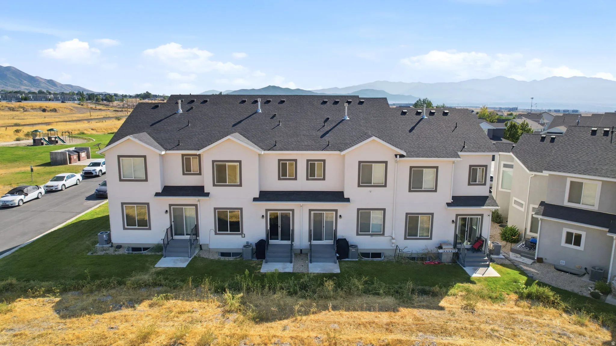 Modern multi-unit residential complex featuring clean-lined architecture with cream and charcoal exterior finishes, dark asphalt shingle roofing, and symmetrical façade design