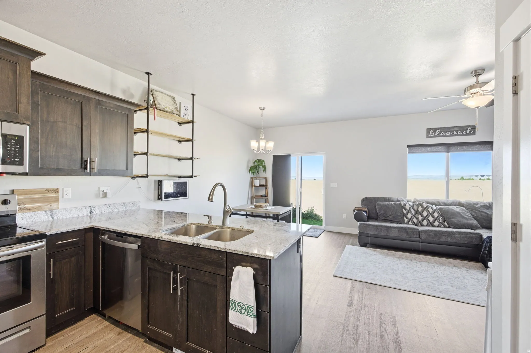 Kitchen island with a double basin sink, stainless steel appliances, dark wood cabinetry, and light granite countertops