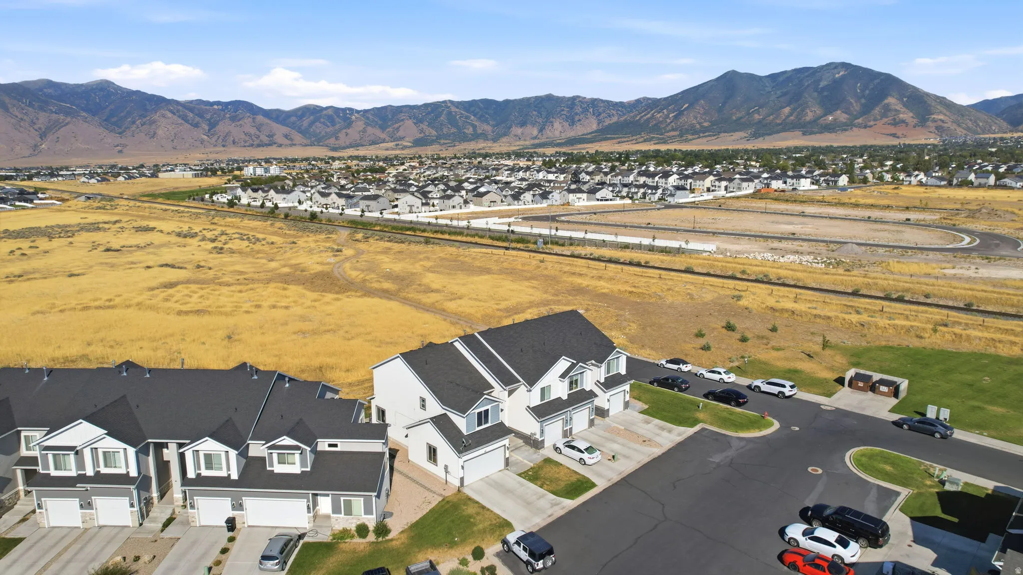 Expansive aerial view showcasing this residence situated on a generous lot with manicured landscaping, paved driveway, and detached garage