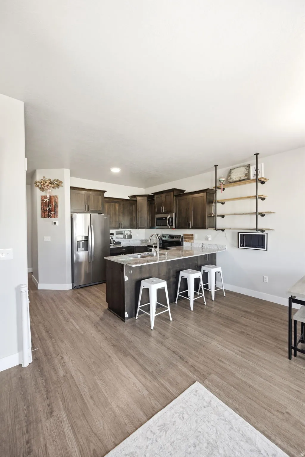 Modern kitchen and dining area featuring stainless steel appliances, dark cabinetry with quartz countertops, and a center island with seating for two