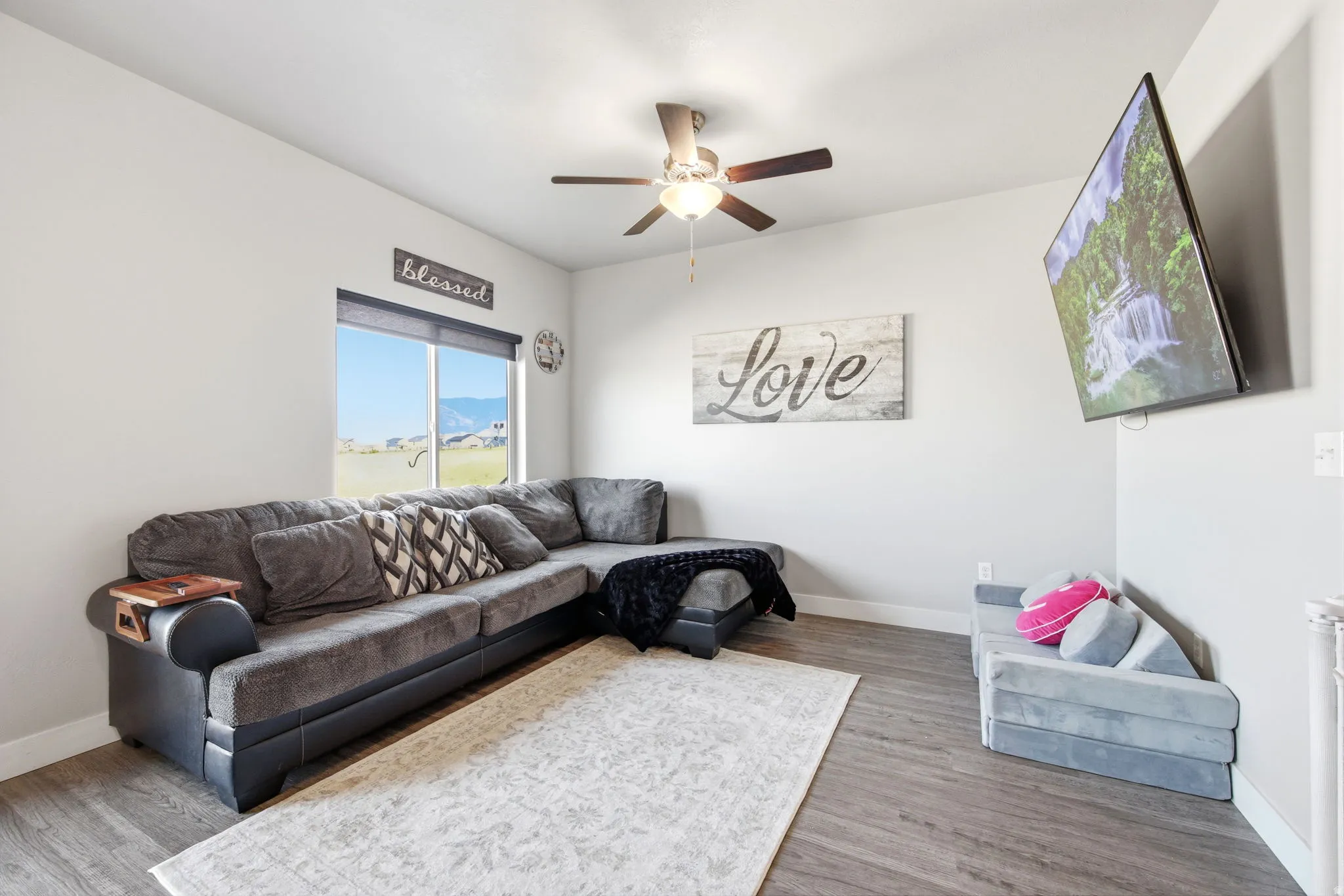 Comfortable living room featuring a sectional sofa, wood-finish flooring, neutral area rug, and ceiling fan with integrated lighting
