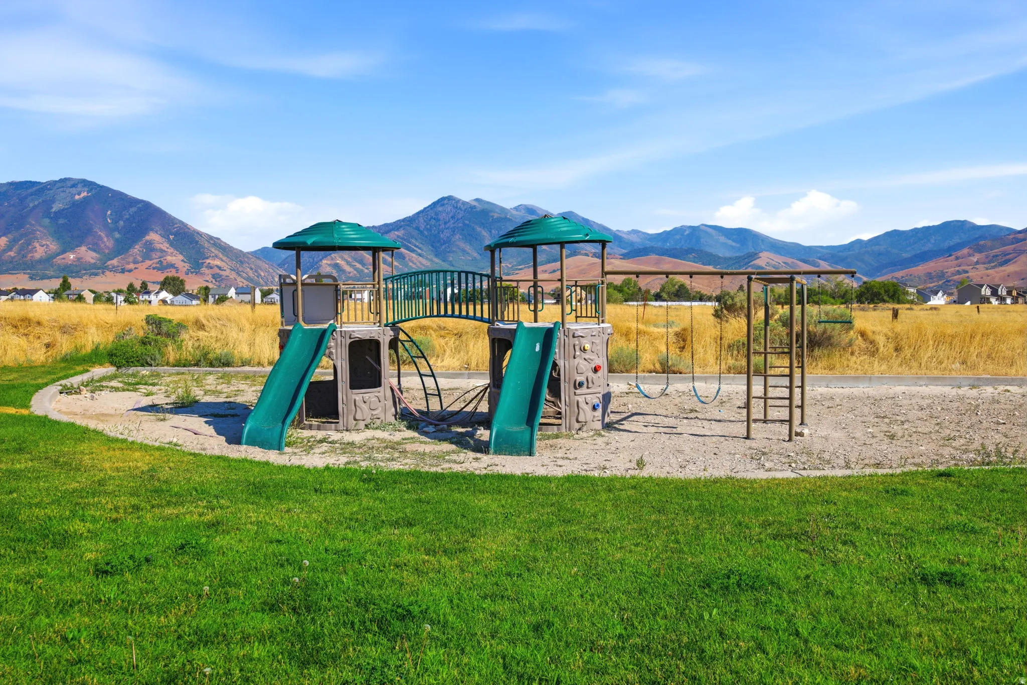 Community playground featuring swings, slides, a climbing wall, and monkey bars, set against a backdrop of distant mountains