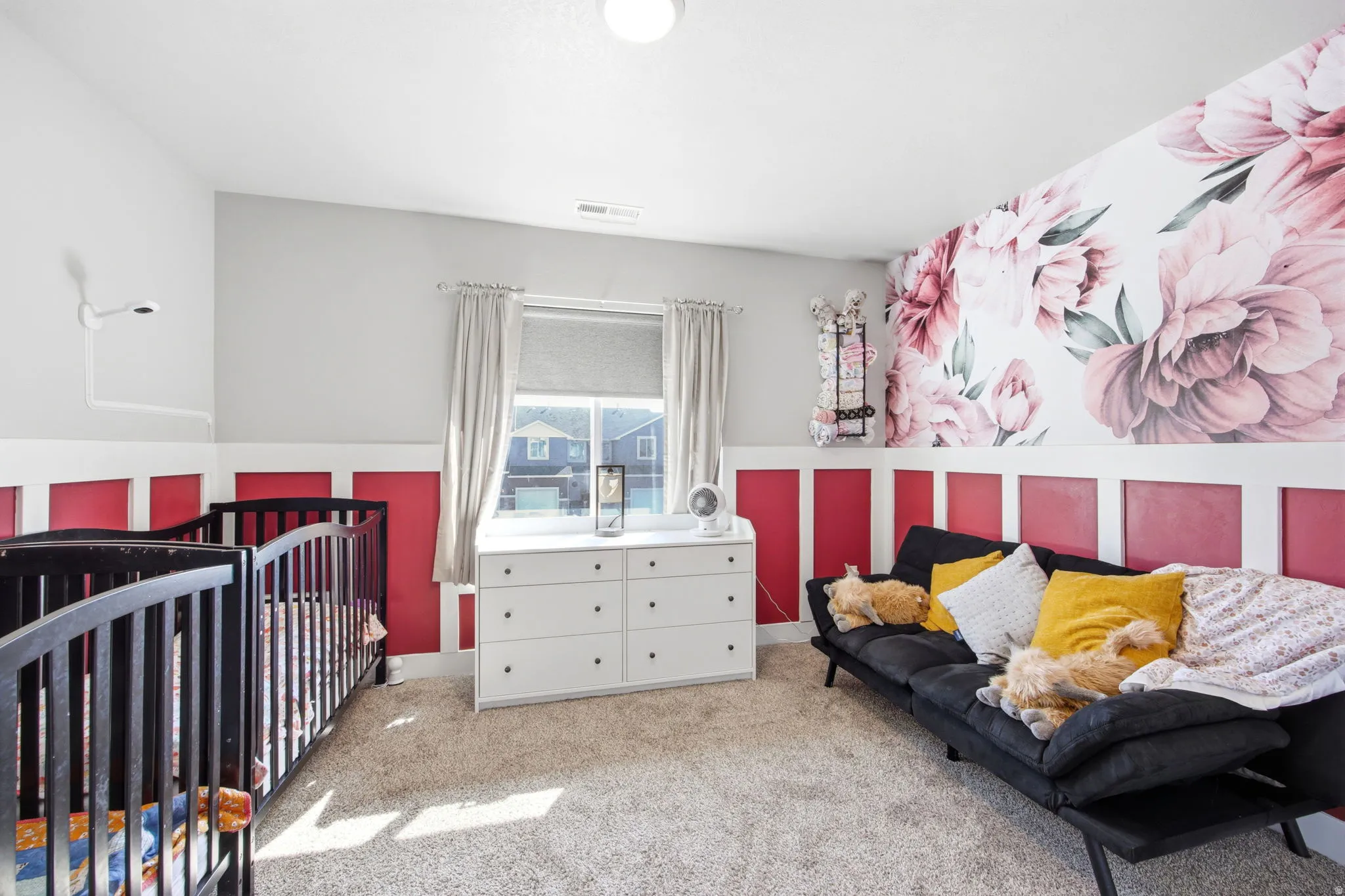 Dual-purpose bedroom and nursery featuring bold red and white striped wainscoting, carpet flooring, and large windows with natural light