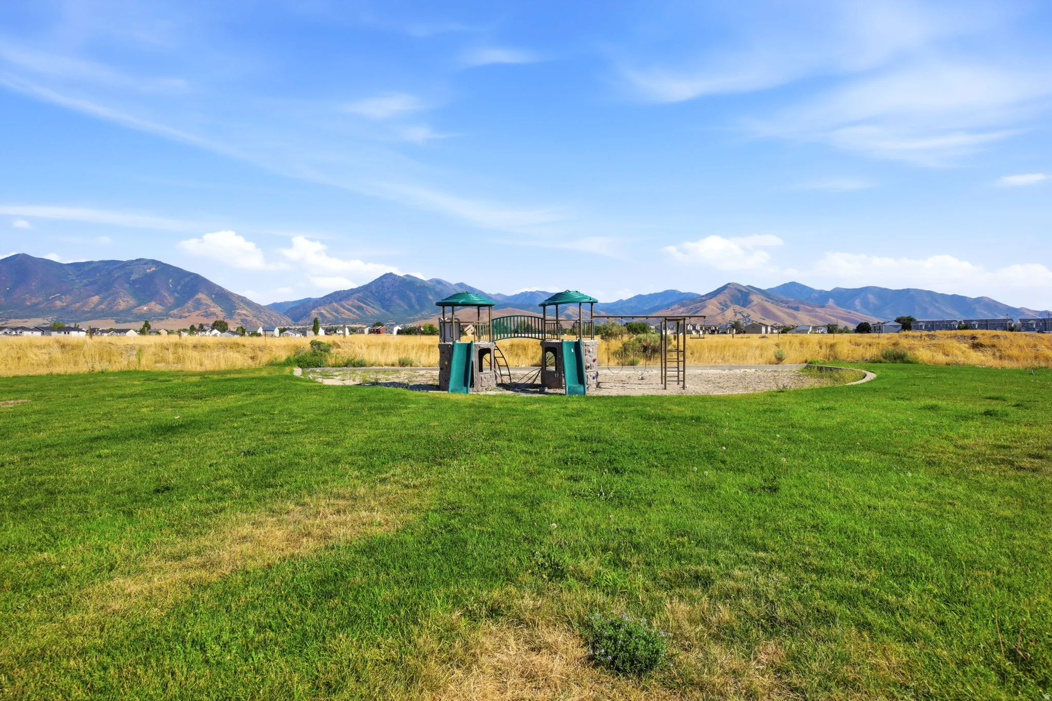 Expansive grounds featuring a manicured lawn with a multi-level playground structure, set against a backdrop of mountain ranges and open countryside