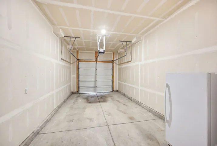 Spacious garage featuring concrete flooring, overhead garage door with automatic opener, wall-mounted basketball hoop, fluorescent ceiling lighting, and finished drywall construction throughout