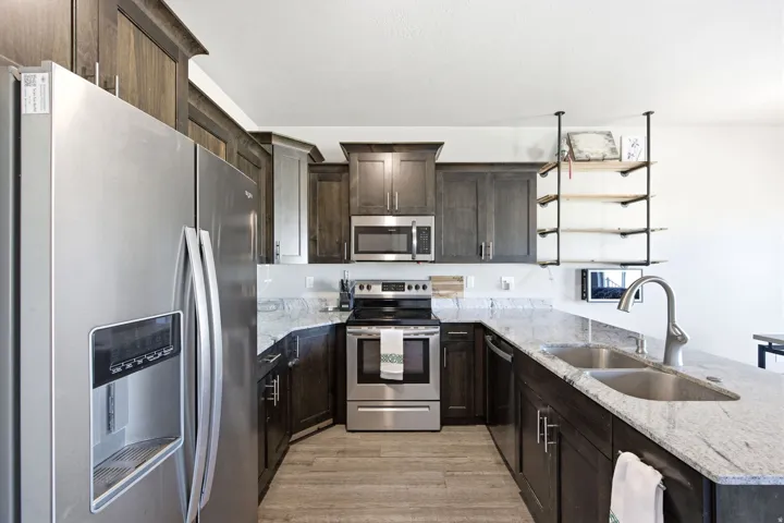 Modern kitchen featuring dark wood cabinetry, stainless steel appliances including a built-in refrigerator and range, and a large island with a gray quartz countertop and undermount sink