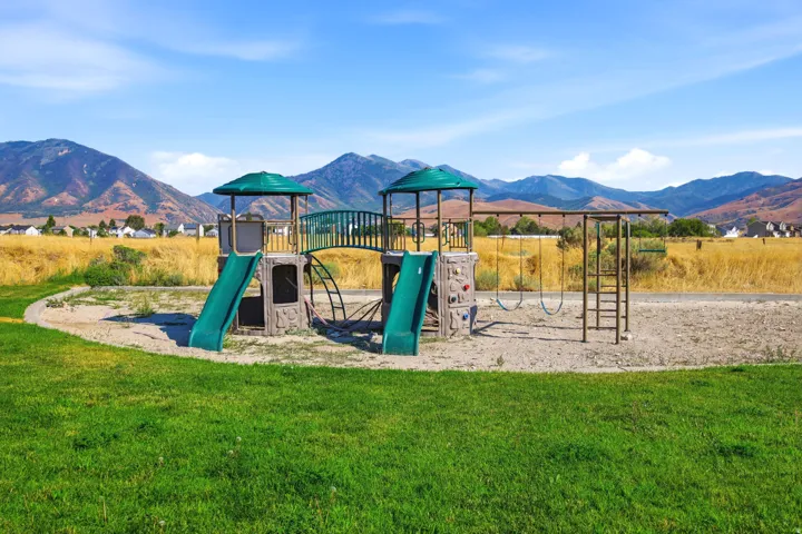 Community playground featuring swings, slides, a climbing wall, and monkey bars, set against a backdrop of distant mountains